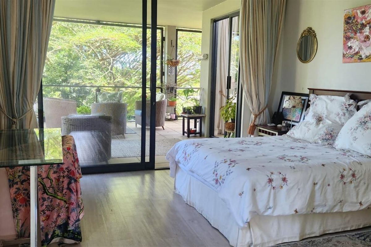 Spacious bedroom featuring laminate flooring and large sliding glass doors that provide direct access to a private balcony with garden views.