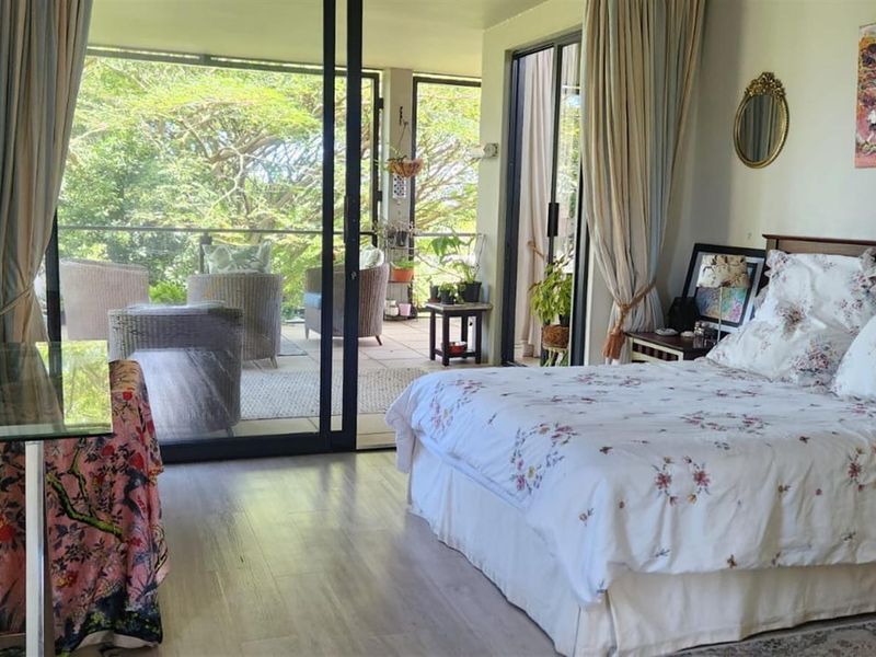 Spacious bedroom featuring laminate flooring and large sliding glass doors that provide direct access to a private balcony with garden views.