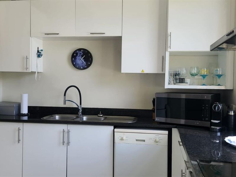 A functional kitchen featuring white cabinetry, contrasting black granite countertops, a stainless steel double sink, and an integrated dishwasher.