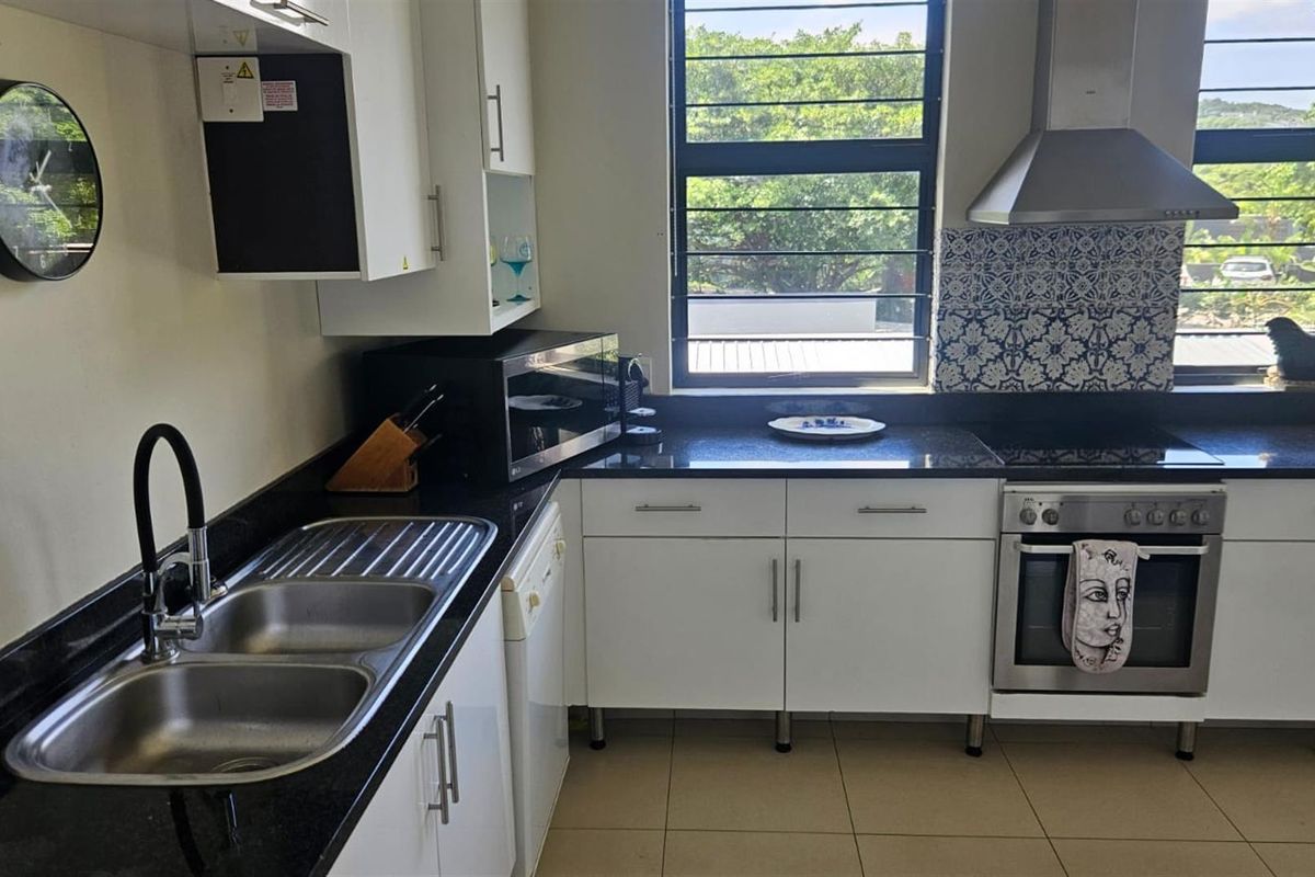 A well-maintained kitchen featuring granite countertops, stainless steel appliances, built-in cabinetry, and a decorative tiled backsplash with ample natural light.