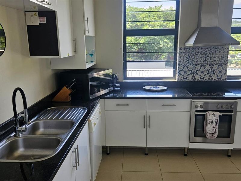 A well-maintained kitchen featuring granite countertops, stainless steel appliances, built-in cabinetry, and a decorative tiled backsplash with ample natural light.