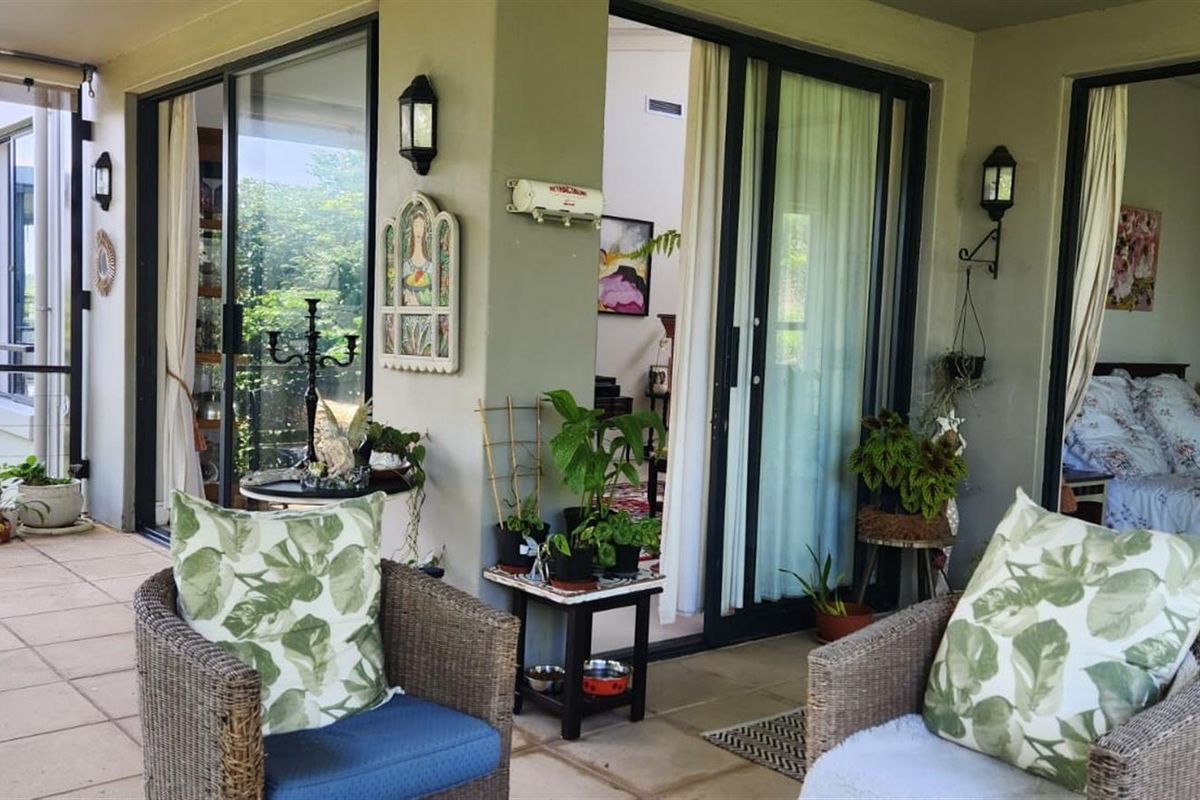 A covered patio area featuring tiled flooring, wall-mounted lighting, and multiple sliding glass door access points to the interior living spaces.