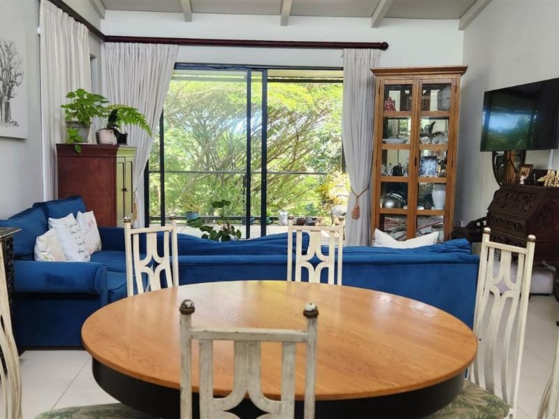 Open plan living and dining area featuring tiled floors, exposed ceiling beams, and large sliding glass doors leading to an outdoor space.