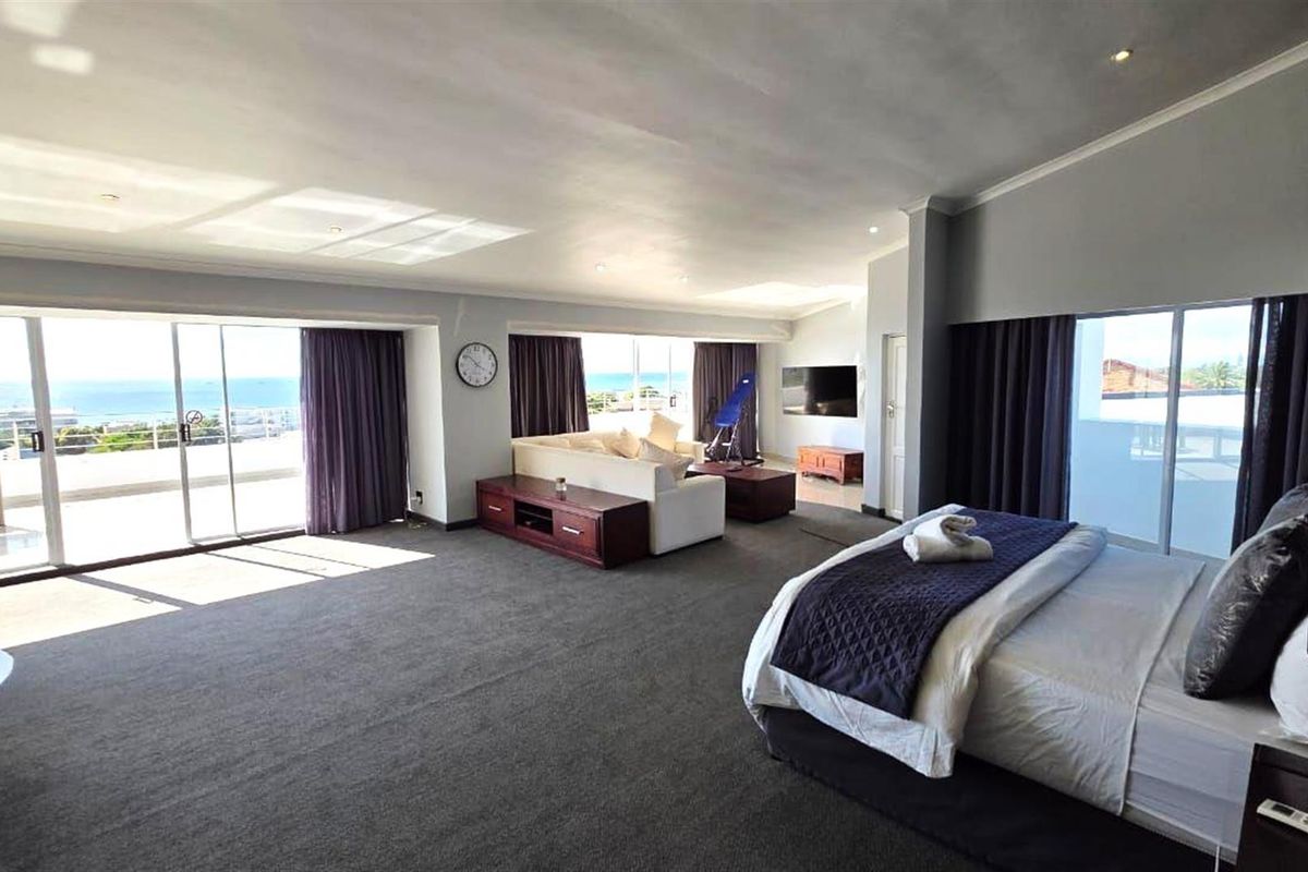 Spacious open-plan bedroom suite featuring large sliding glass doors, neutral carpeting, and direct access to a private balcony with ocean views.