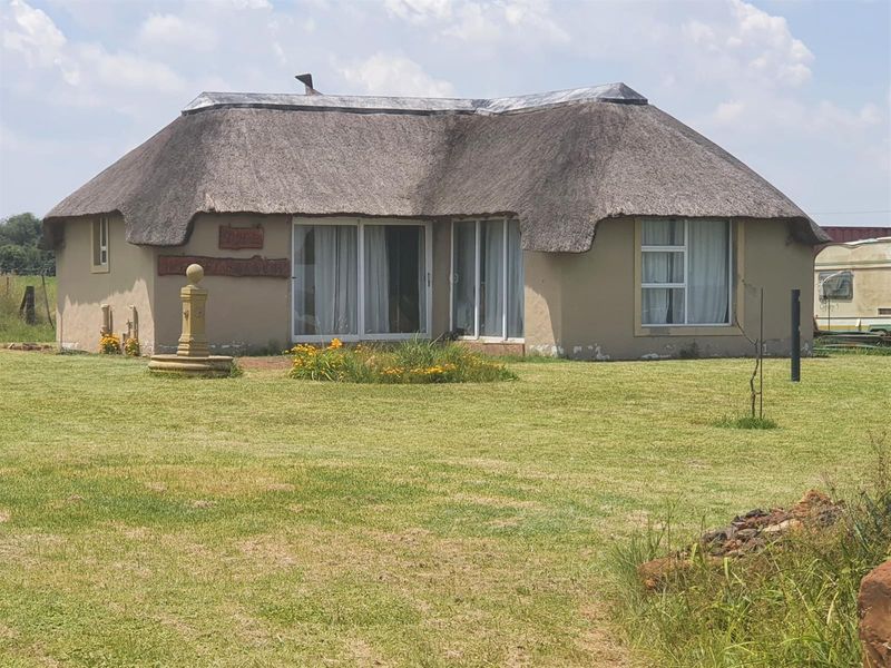 A single-story farmhouse featuring a traditional thatched roof, sliding glass doors, and a stone fountain set within a spacious garden.