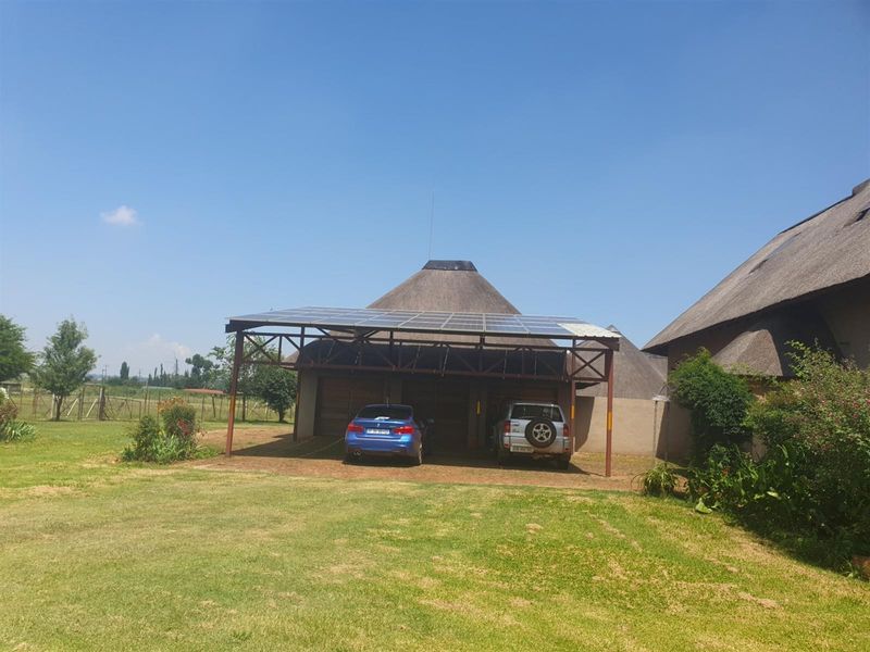 A detached garage structure featuring a thatched roof and a solar panel array mounted on a metal carport frame.