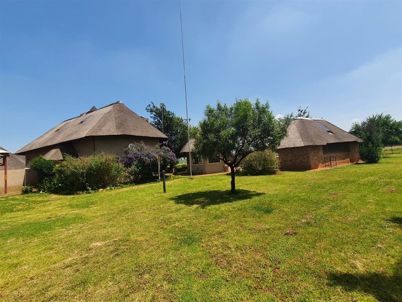 A view of the rear garden featuring multiple structures with traditional thatch roofing and brick exterior walls set within a spacious lawn area.