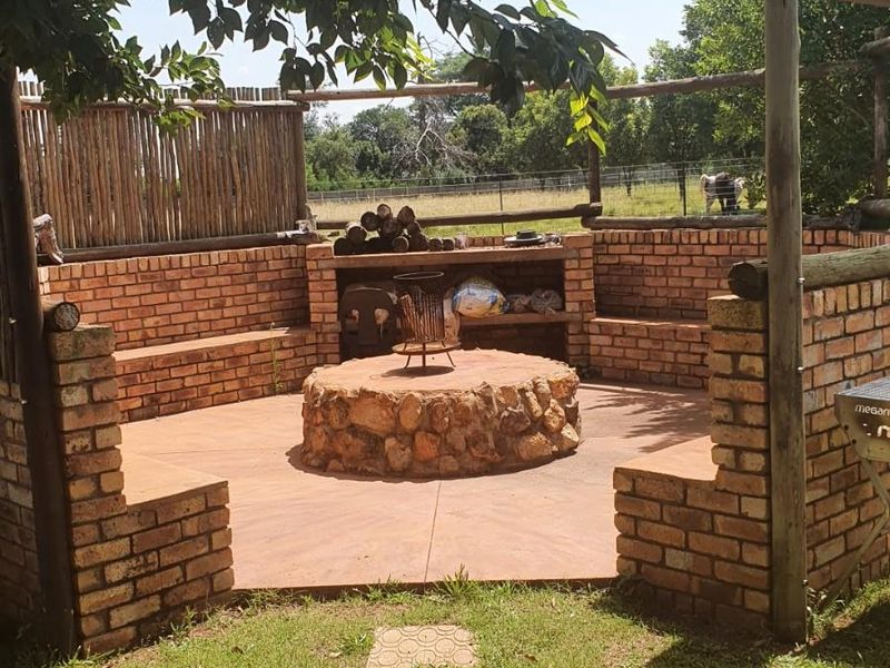 Outdoor entertainment area featuring a built-in brick braai, stone fire pit, and integrated brick seating under a timber pergola structure.