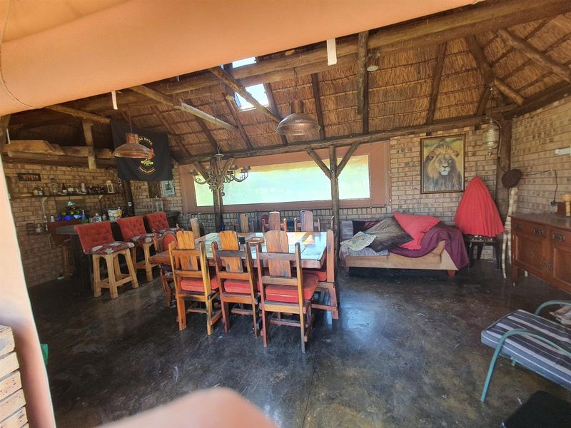 Spacious covered outdoor entertainment area featuring a rustic thatched roof, exposed timber trusses, brick walls, and a built-in bar, ideal for farm-style gatherings.