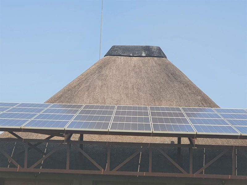 A close-up view of a traditional thatch roof structure featuring an integrated solar panel array mounted on a metal support frame.