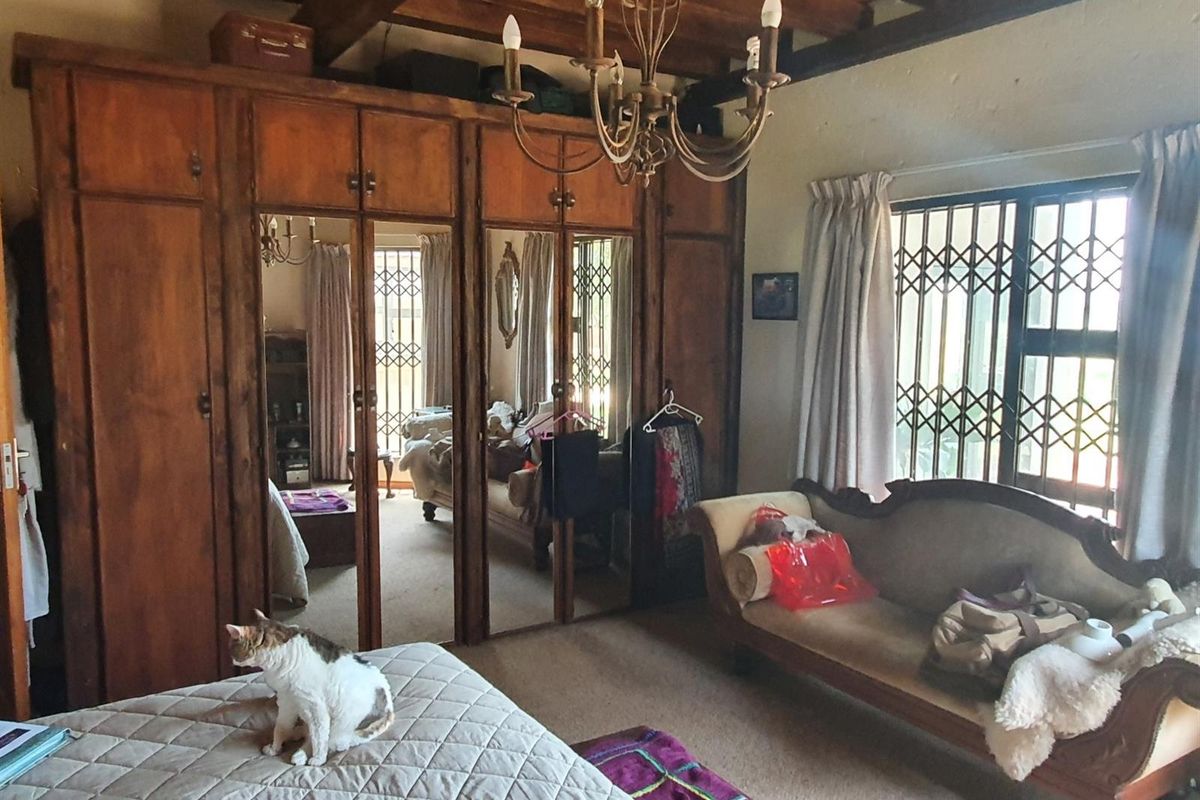 Spacious bedroom featuring exposed timber ceiling beams, extensive built-in wooden wardrobes with mirrored panels, and secure wrought iron window gates.