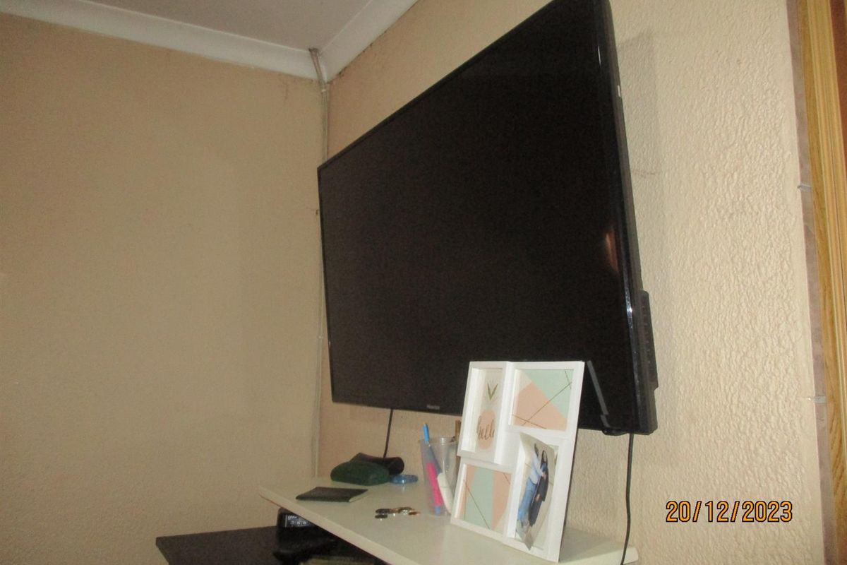 A close-up view of a wall-mounted television in a living area, featuring textured wall finishes and visible surface-mounted wiring.