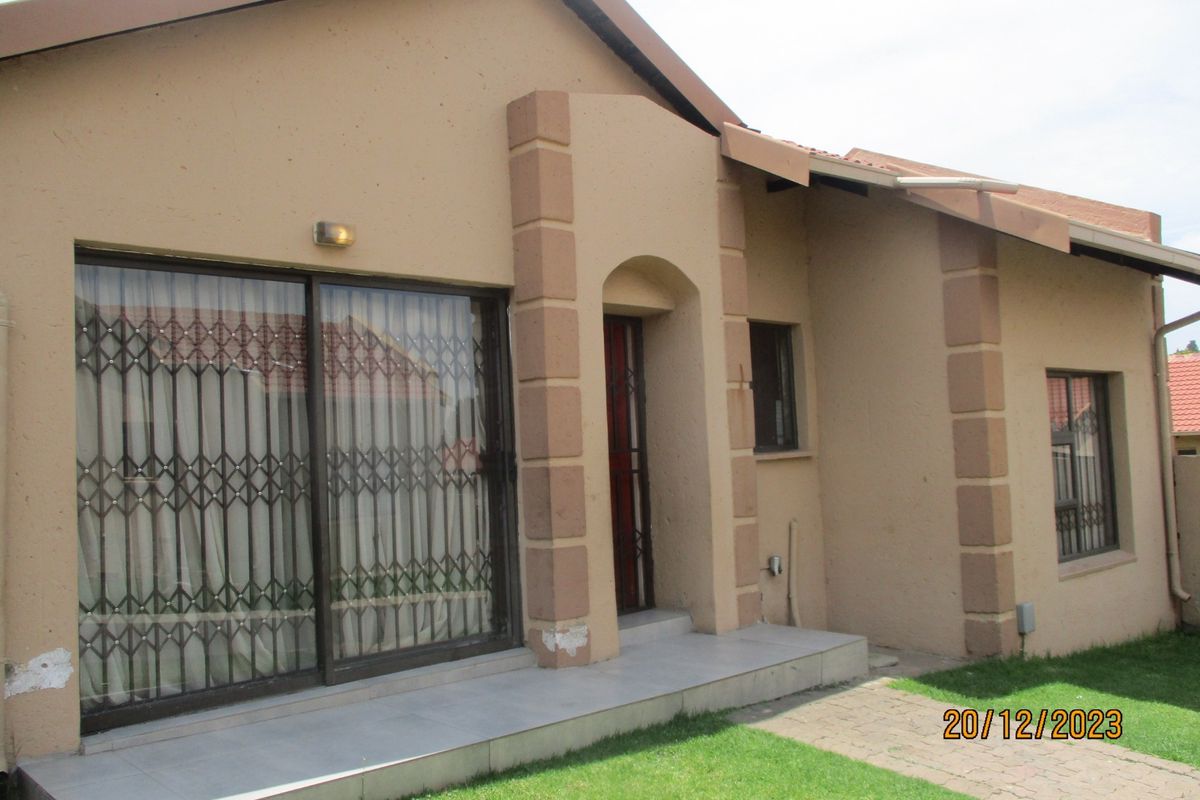 Exterior view of the house featuring a tiled patio, sliding glass door with security gate, and paved walkway leading to the entrance.