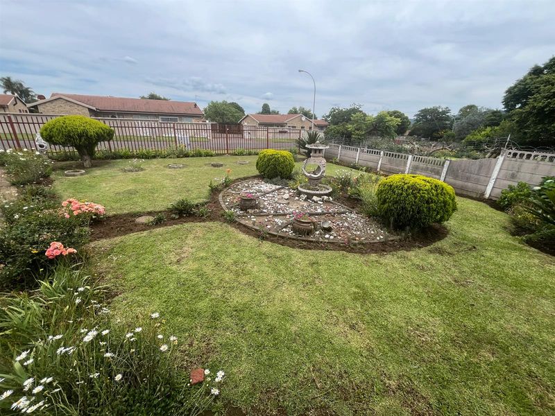 A well-maintained residential garden featuring a central landscaped bed, manicured shrubs, and secure perimeter fencing.