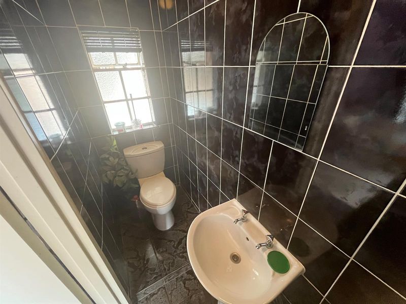 A compact bathroom featuring dark wall and floor tiles, a white pedestal basin, and a standard toilet.