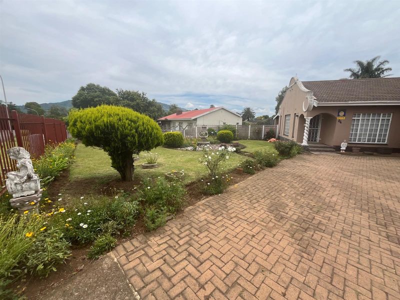 A well-maintained front garden featuring a paved driveway, manicured lawn, established shrubs, and a decorative fountain, leading to the main entrance of the house.