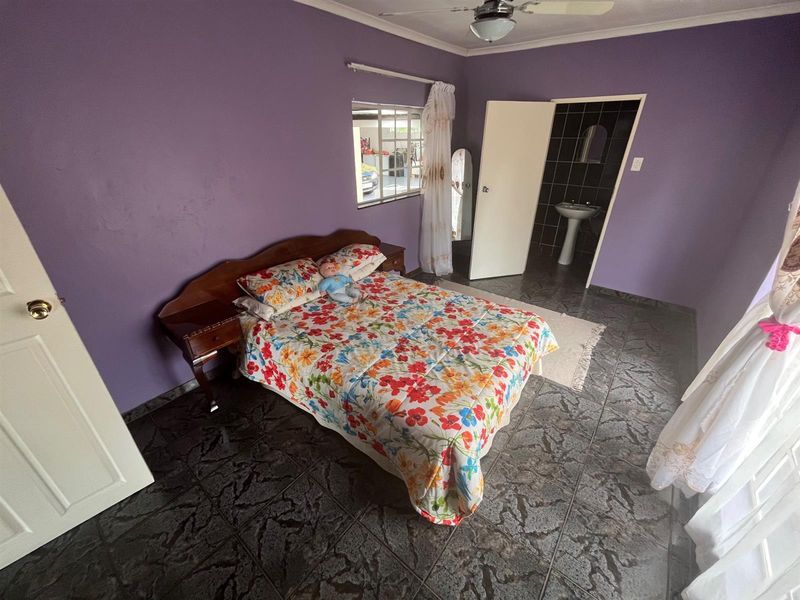 A bedroom featuring dark tiled flooring, purple walls, and an en-suite bathroom with a pedestal basin.