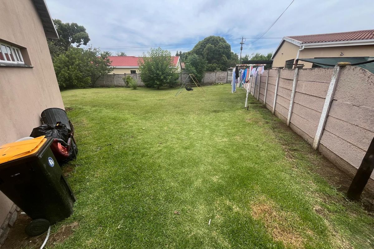 A spacious rear garden featuring a large lawn area enclosed by concrete boundary walls.