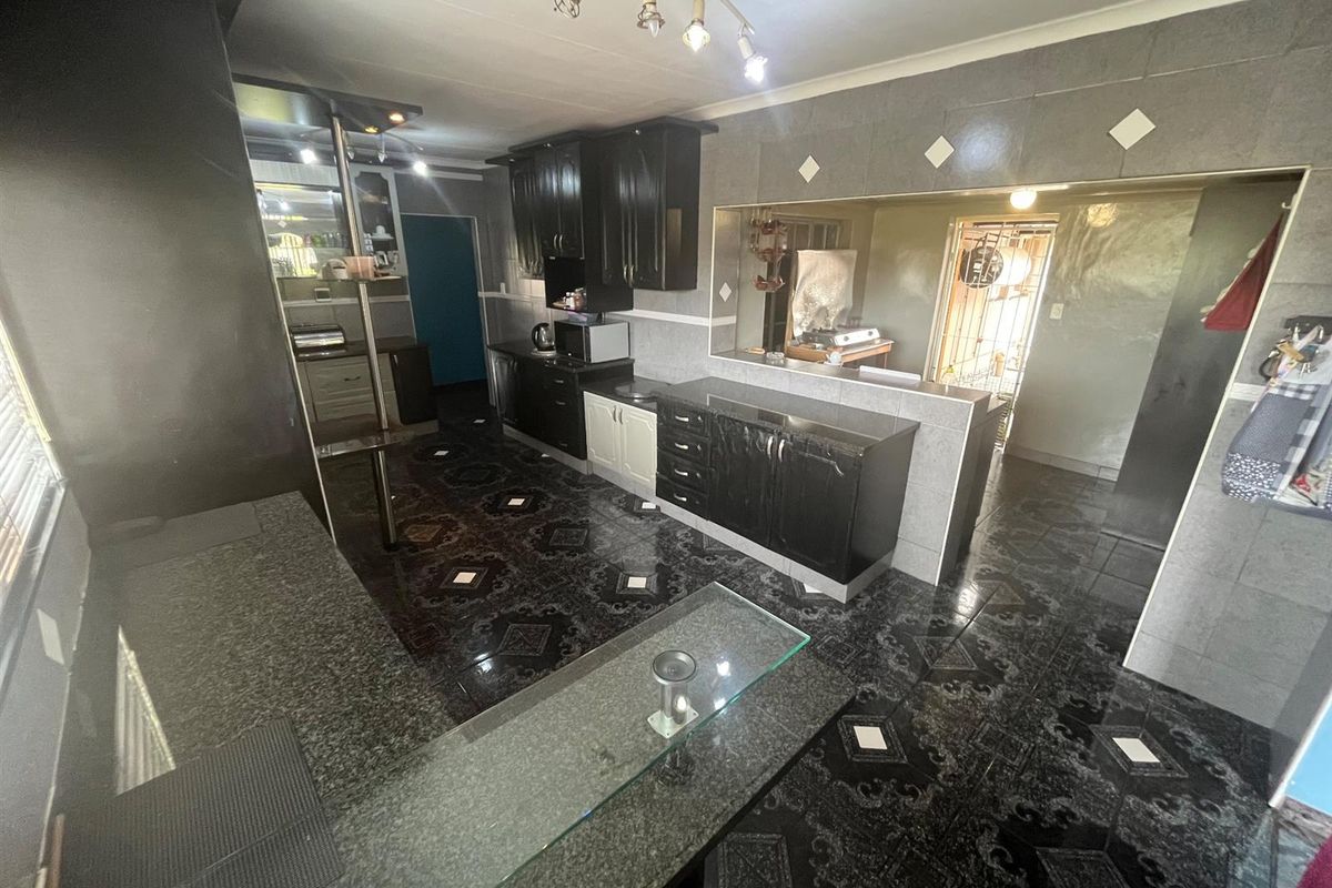 A spacious kitchen featuring dark cabinetry, granite-style countertops, and patterned floor tiles with a breakfast bar area connecting to an adjacent room.