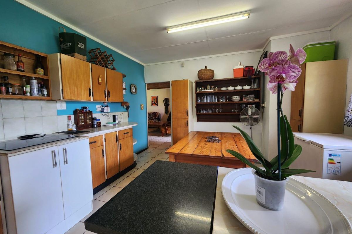 A functional kitchen featuring wooden cabinetry, tiled flooring, and a built-in hob, with an open-plan layout leading into the adjacent living area.