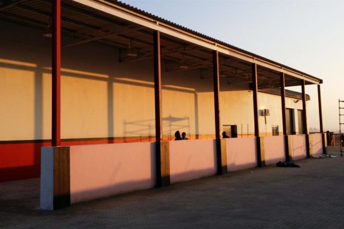 Exterior view of an industrial building featuring a covered walkway, steel support columns, and paved ground area.