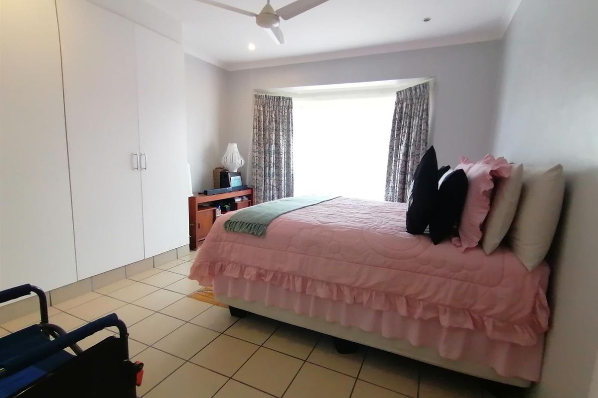 A well-lit bedroom featuring tiled flooring, a ceiling fan, and built-in cupboards, with a bay window providing natural light.