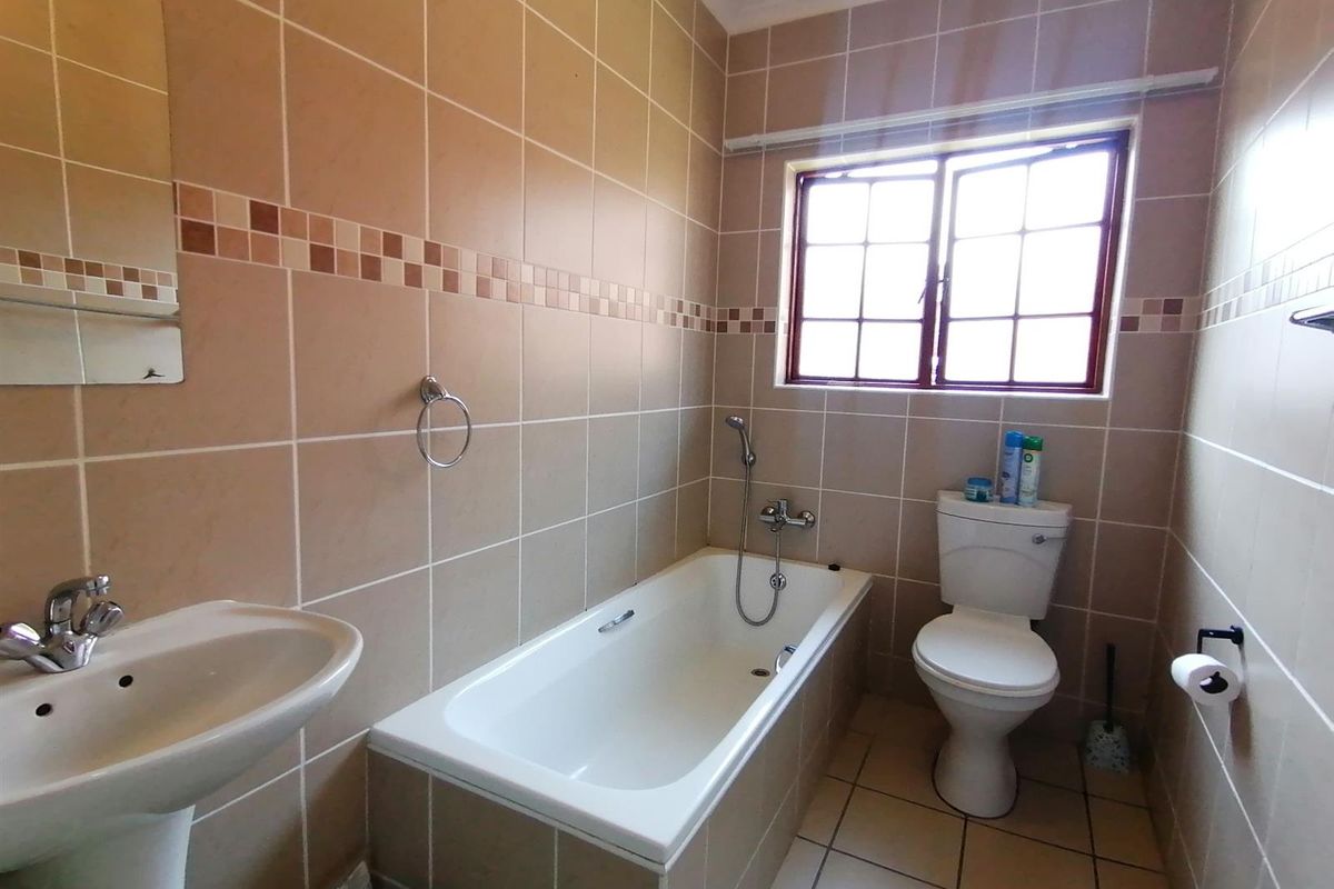 A functional bathroom featuring a pedestal basin, a built-in bathtub with a handheld shower mixer, and a toilet, finished with neutral wall and floor tiles.