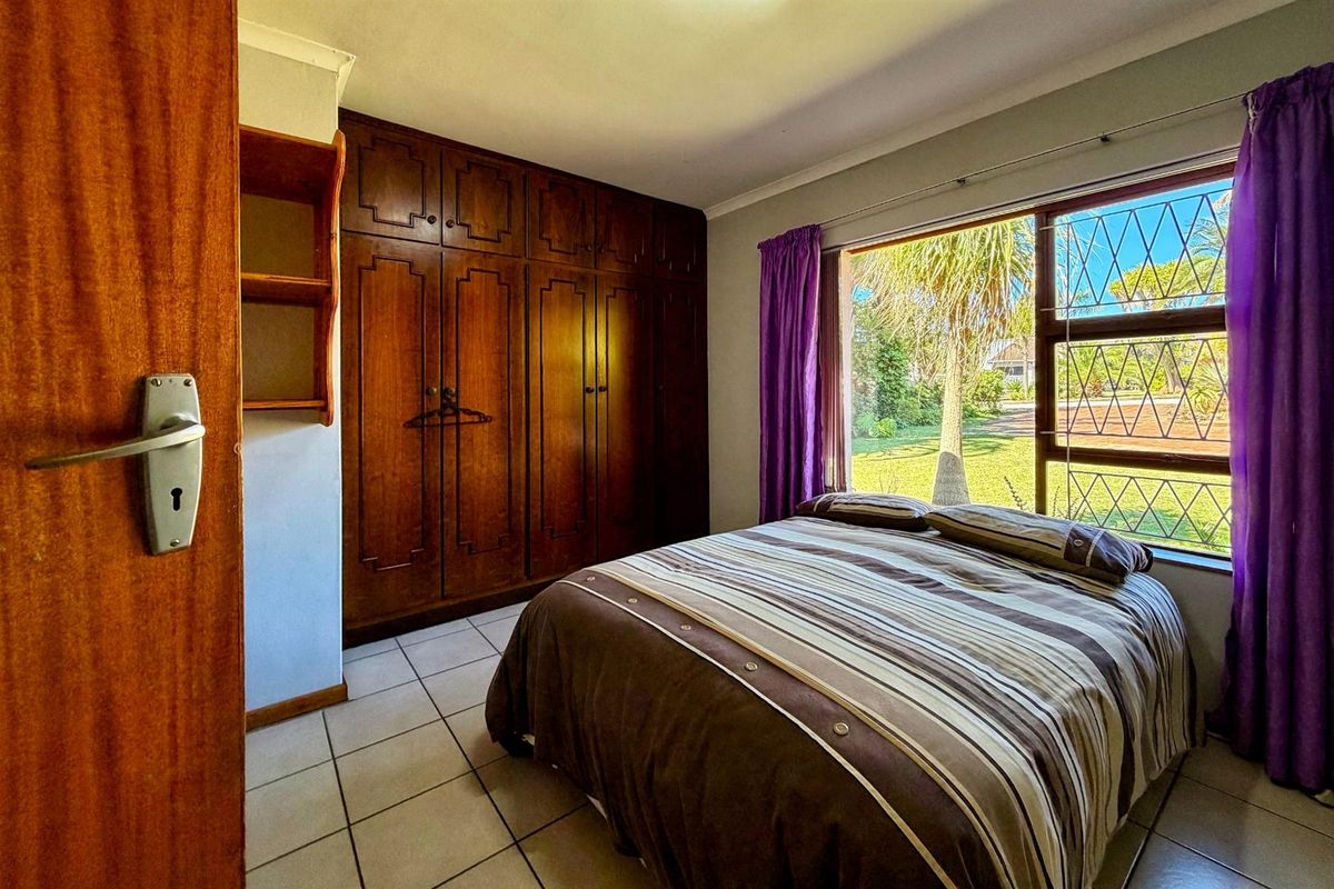 A bedroom featuring built-in wooden cabinetry, tiled flooring, and a large window providing natural light and garden views.