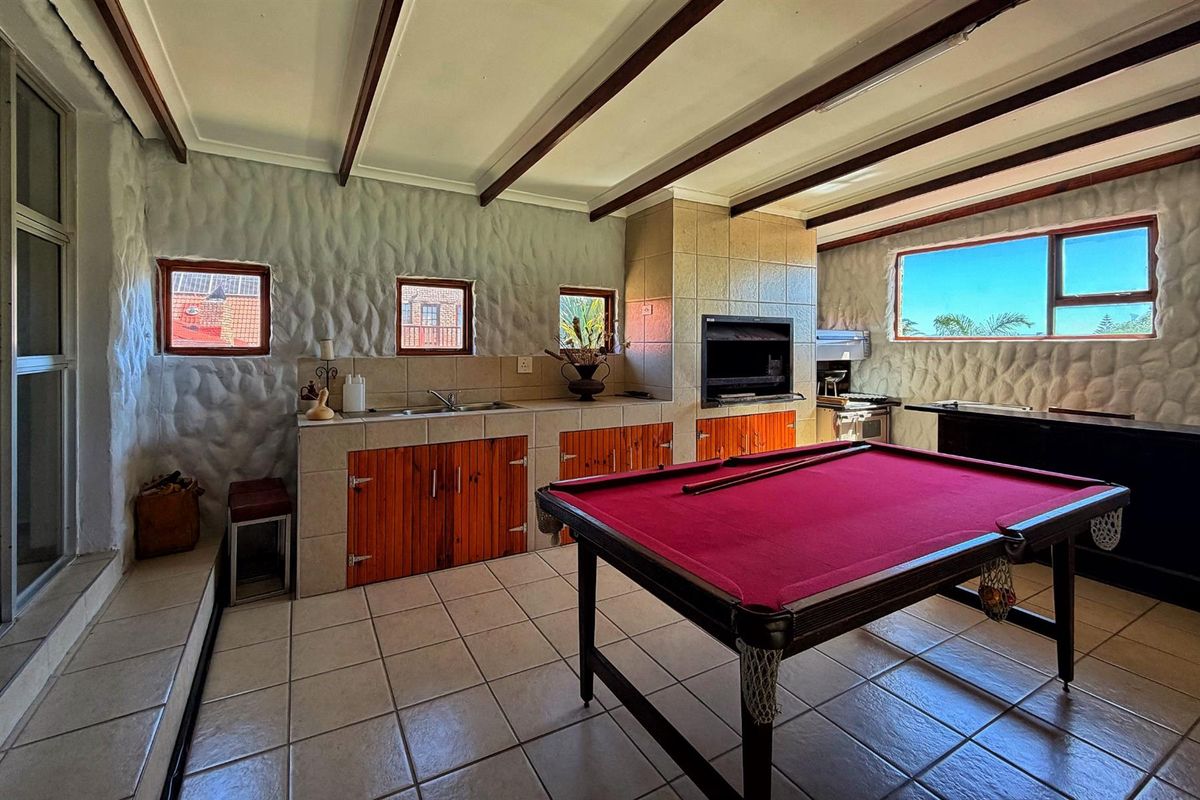 Spacious entertainment area featuring exposed timber ceiling beams, tiled flooring, built-in cabinetry with sink, and a built-in braai for indoor social gatherings.