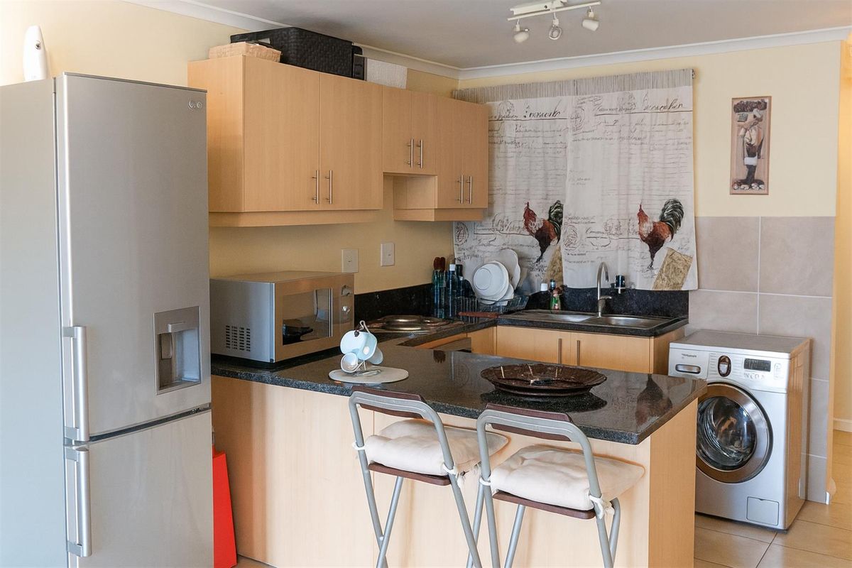 A functional kitchen featuring light wood cabinetry, dark granite countertops, a double sink, and integrated space for a washing machine.