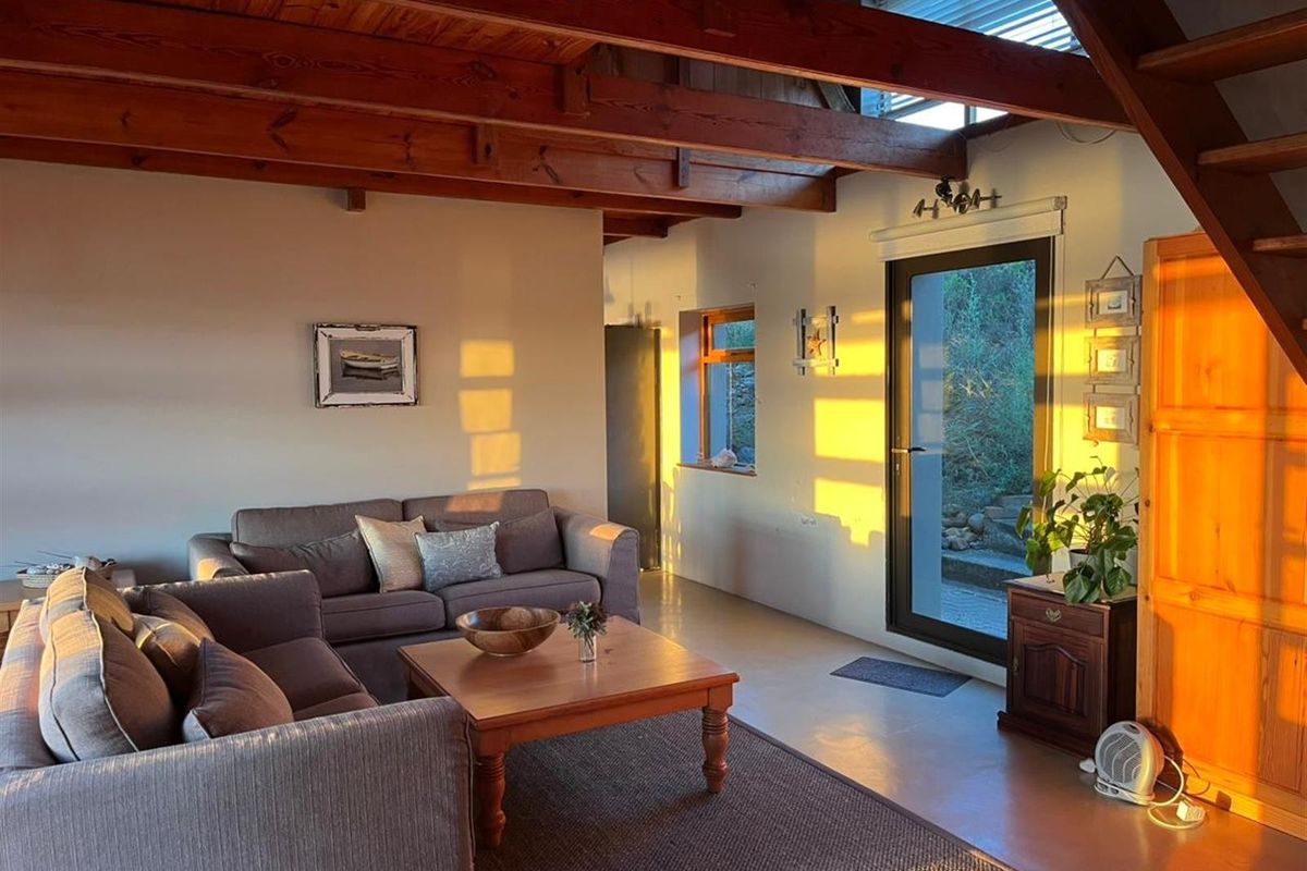 A cozy living room featuring exposed timber ceiling beams, polished concrete flooring, and a glass door providing direct access to the outdoor area.