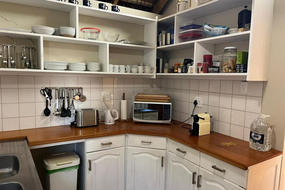A functional kitchen corner featuring white cabinetry, wooden countertops, tiled splashbacks, and open shelving under a rustic thatched roof structure.