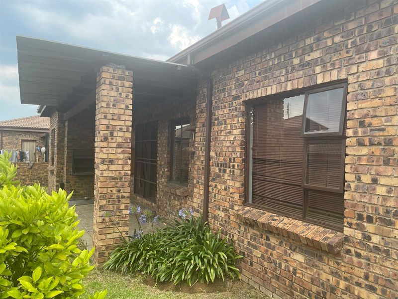 Rear exterior view of the penthouse featuring a face brick facade, a covered patio area with a built-in braai, and aluminium window frames.
