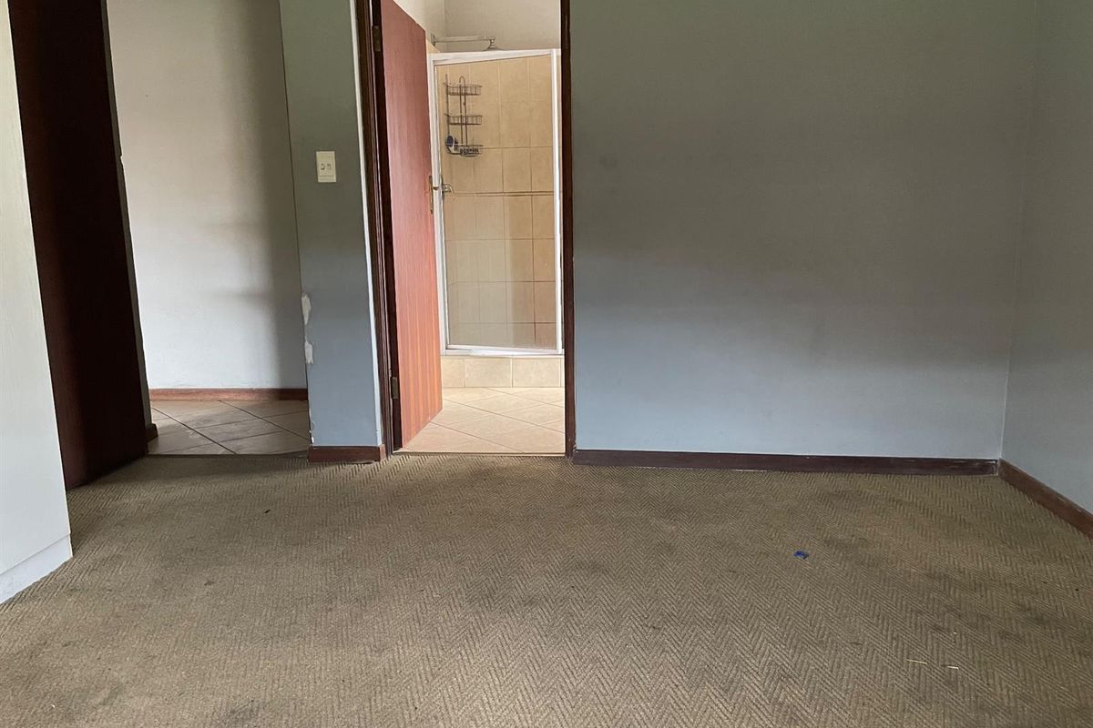 An empty bedroom featuring worn carpeting and direct access to an en-suite bathroom with a shower enclosure.
