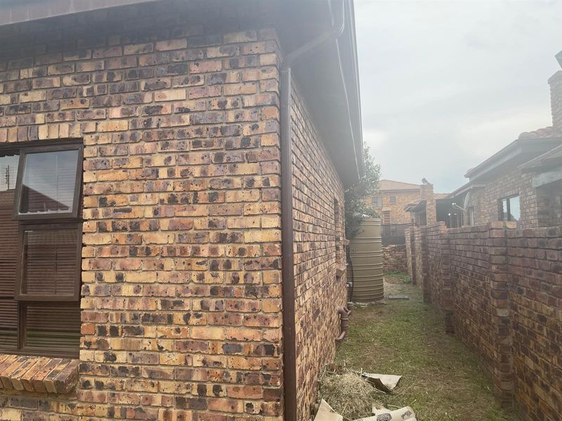 A view of the rear exterior of the property featuring face brick walls, a rainwater storage tank, and a side garden path.