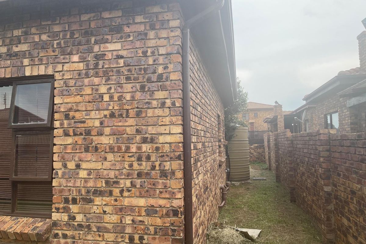 A view of the rear exterior of the property featuring face brick walls, a rainwater storage tank, and a side garden path.