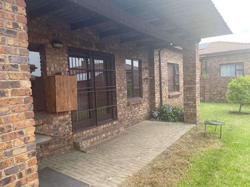 Covered brick patio area with paved flooring and security gates, offering direct access to the garden space.