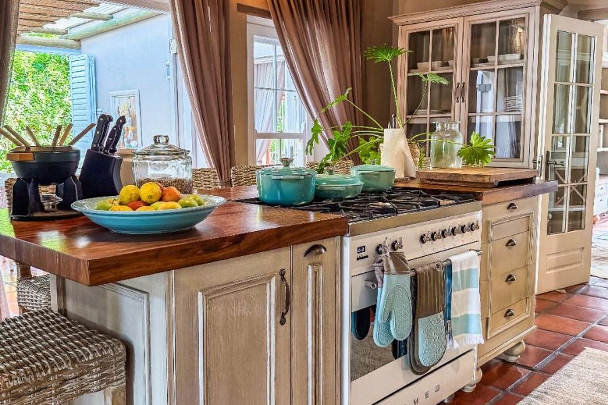 A rustic-style kitchen featuring a central island with a wooden countertop, a Smeg range cooker, exposed timber ceiling beams, and terracotta floor tiles.