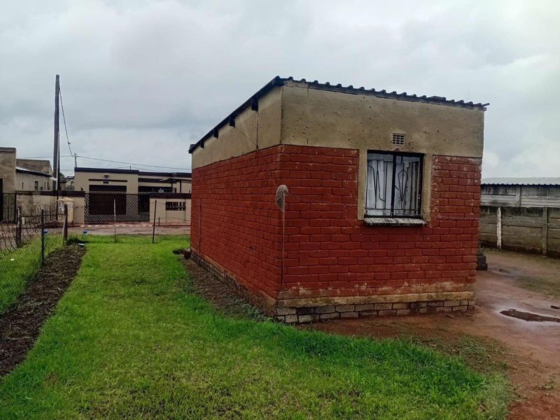 A detached brick outbuilding structure featuring a corrugated roof and security-barred window, situated on a residential plot.