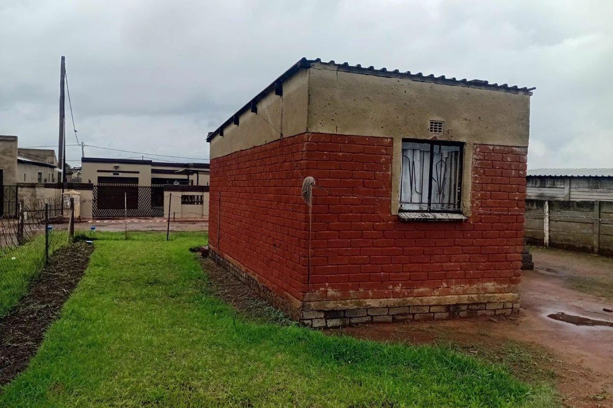 A detached brick outbuilding structure featuring a corrugated roof and security-barred window, situated on a residential plot.