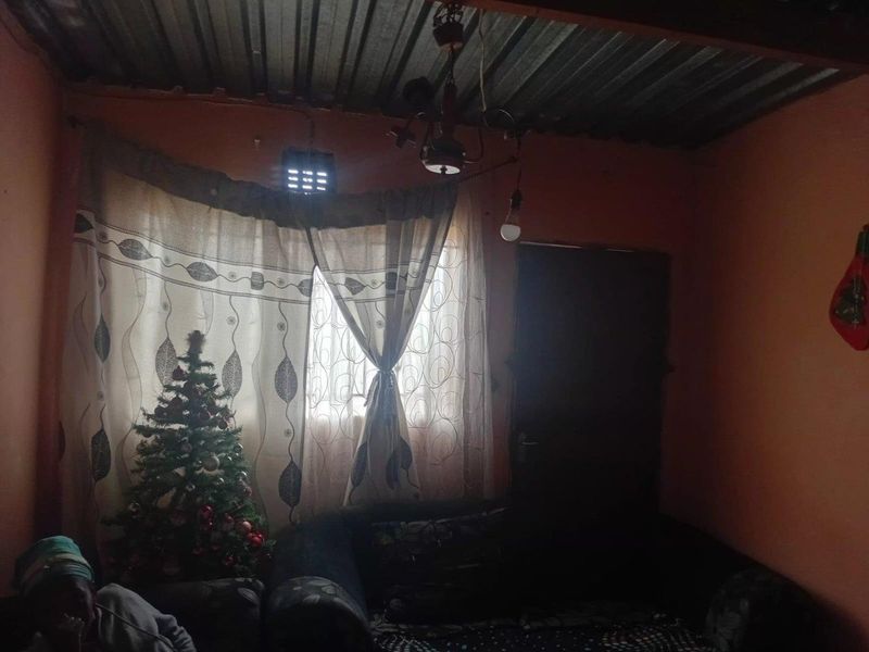 A basic living area featuring exposed corrugated metal roofing and simple wall finishes, providing a functional but dated interior space.