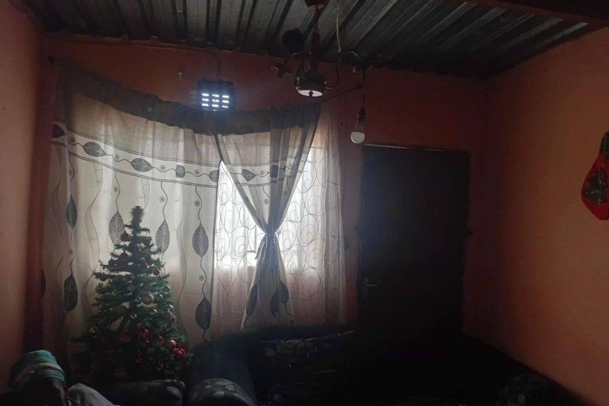 A basic living area featuring exposed corrugated metal roofing and simple wall finishes, providing a functional but dated interior space.