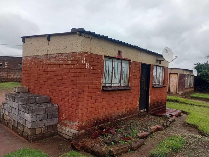 A modest single-story detached house featuring exposed brick construction, metal window security bars, and a corrugated roof.