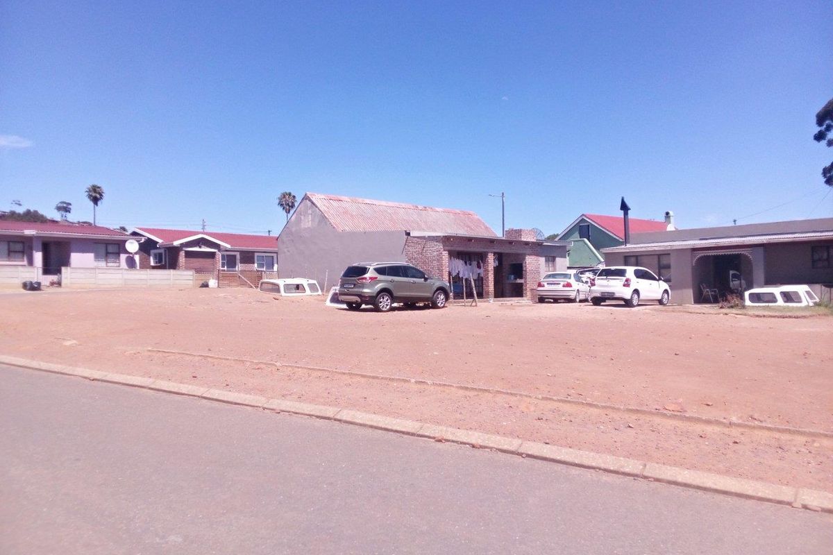 Street view of a residential property featuring an unpaved front yard area and existing dwelling structures with corrugated metal roofing.