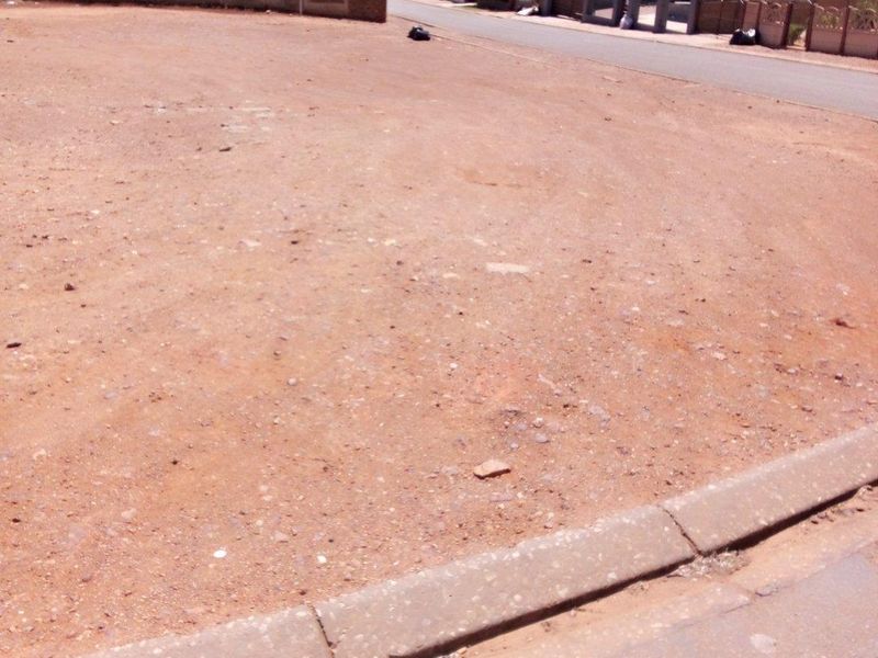 A vacant residential plot of land situated in a suburban street, featuring a level surface and clear access from the paved road.