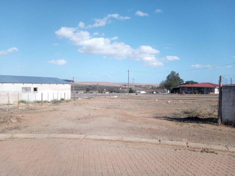 A vacant residential plot featuring an open, level landscape with surrounding boundary fencing and nearby established structures.