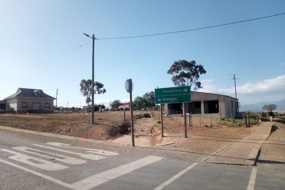 A view of a vacant residential plot situated at a street corner, featuring nearby utility poles and local road signage.