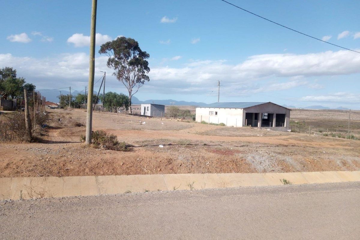 A view of a vacant residential plot featuring an unfinished outbuilding structure and basic utility connections in a rural setting.