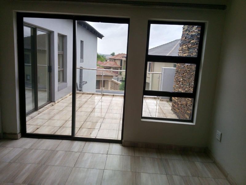 An interior view of a room featuring large sliding glass doors that open onto a tiled balcony with a stone-clad feature wall.