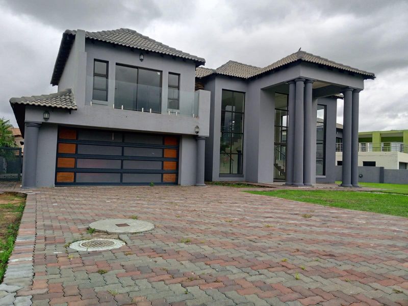 Modern double-story residential home featuring a grey facade, integrated garage, large glass windows, and a grand entrance with classical columns.